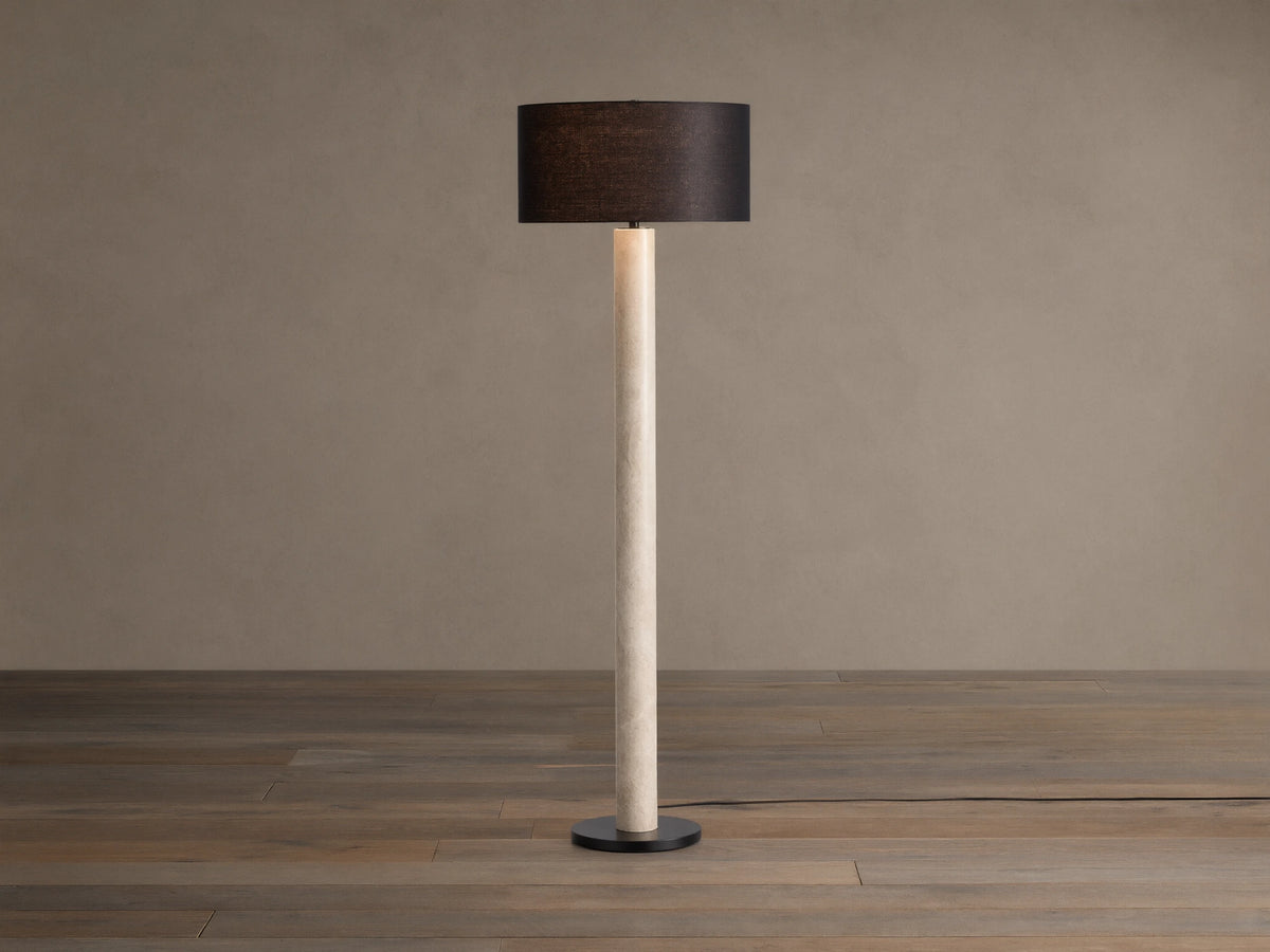 Brixton Floor Lamp with tall light marble-patterned column, dark cylindrical shade, and black round base. Against a plain wall.