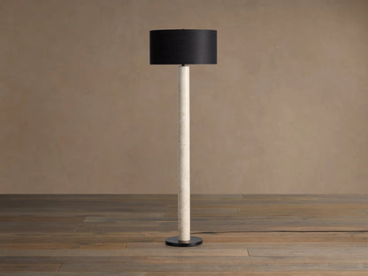 Brixton Floor Lamp with tall light marble-patterned column, dark cylindrical shade, and black round base. Against a plain wall.