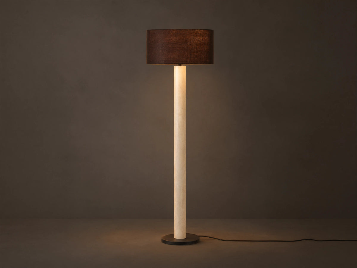 Brixton Floor Lamp with tall light marble-patterned column, dark cylindrical shade, and black round base. Against a plain wall.