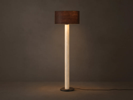Brixton Floor Lamp with tall light marble-patterned column, dark cylindrical shade, and black round base. Against a plain wall.