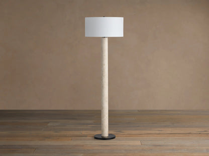 Brixton Floor Lamp with a tall, light beige marble-look stem, white cylindrical shade, and round black base on a wood floor.