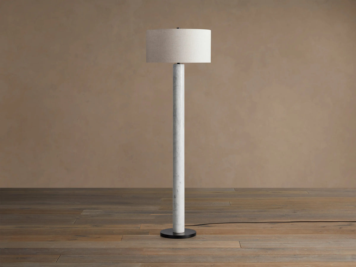 Brixton Floor Lamp with white marble column, light fabric drum shade, and black base, on wood floor against warm wall.
