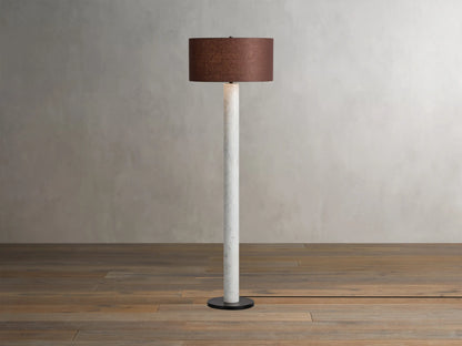 Brixton Floor Lamp with a slender white marble column, dark round base, and a brown fabric drum shade on a wooden floor.