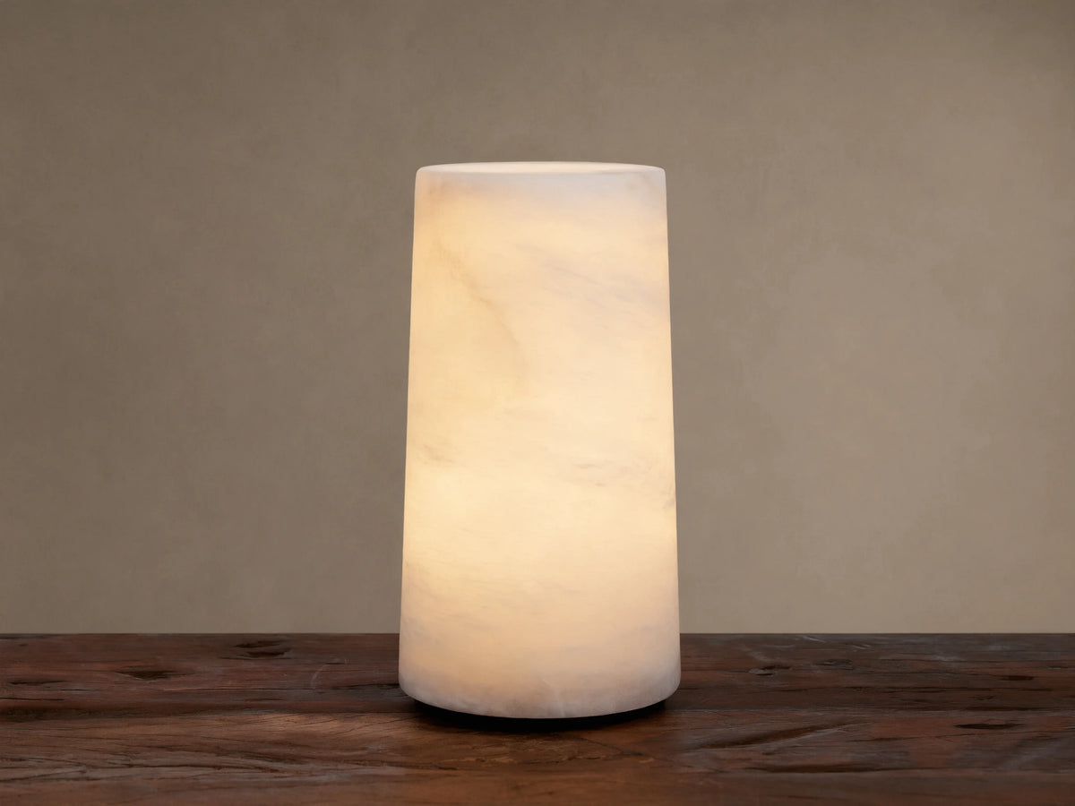 Kelby Outdoor Rechargeable Lamp: Glowing cylindrical alabaster lamp with natural veining, sitting on a rustic wooden table.
