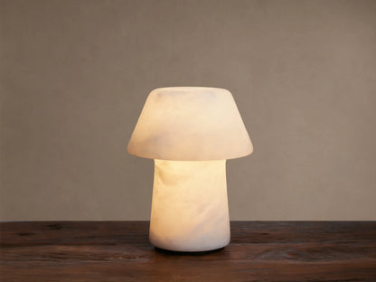 Daine Alabaster Outdoor Rechargeable Table Lamp, mushroom-shaped, glowing milky white, on rustic wood against brown wall.