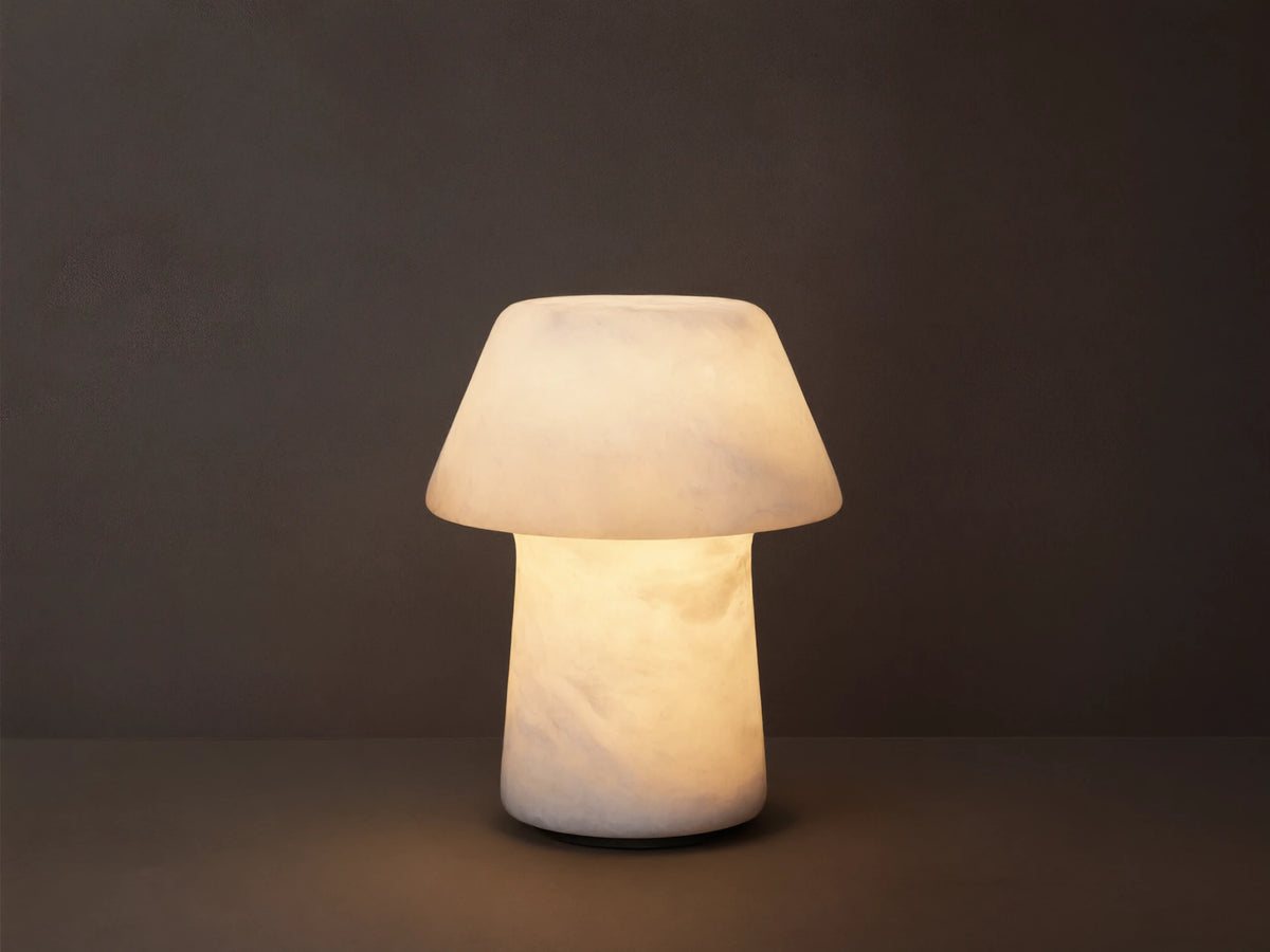 Daine Alabaster Outdoor Rechargeable Table Lamp, mushroom-shaped, glowing milky white, on rustic wood against brown wall.
