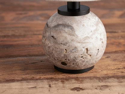 Celia Outdoor Rechargeable Lamp with a round grey textured stone base, black hardware, and flax linen conical shade on a wooden table.