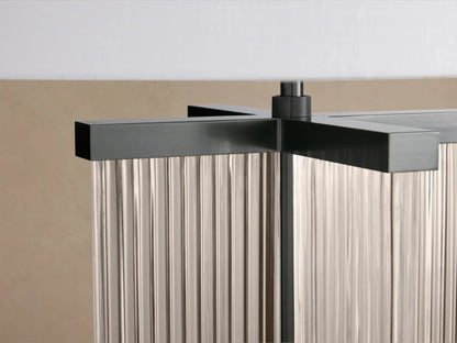 Delsie Table Lamp with a clear ribbed glass base, dark metal accents, and a white drum shade, on a wooden table.
