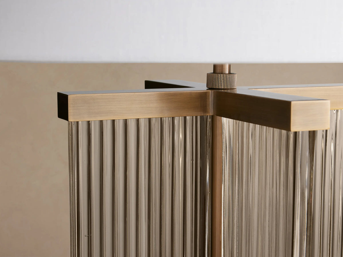 Delsie Table Lamp with white cylindrical shade, fluted glass and burnished brass base, on a rustic wooden table.