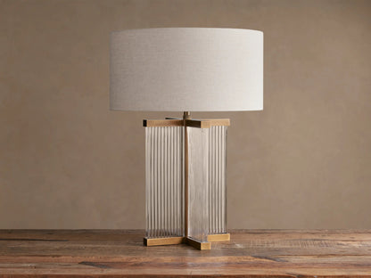 Delsie Table Lamp with flax linen shade, fluted glass base, and burnished brass accents on a rustic wooden surface.