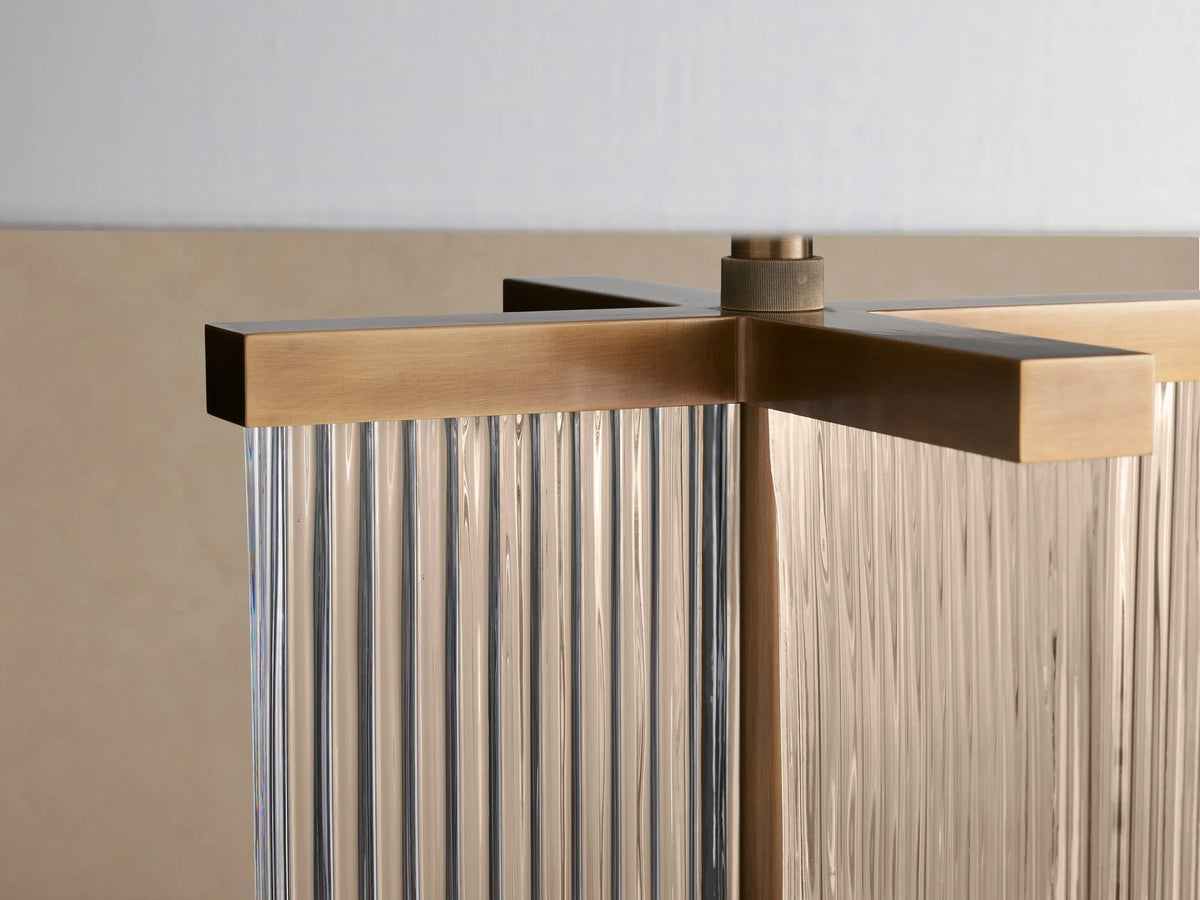 Delsie Table Lamp featuring a white drum shade, clear fluted glass base, and burnished brass accents, on a rustic wooden table.