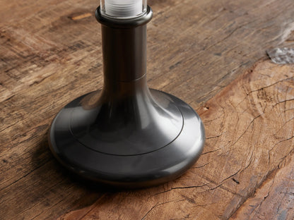 Luella Outdoor Rechargeable Lamp with a slender glass cylinder atop a brushed bronze base on a wooden surface.