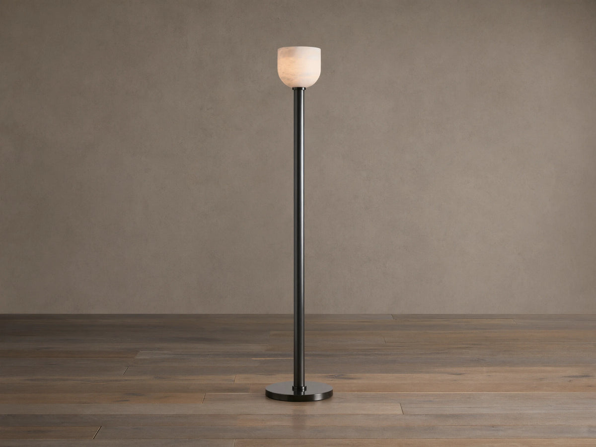 Ansley Floor Lamp: tall, dark steel pole and round base with an illuminated natural alabaster stone shade on a wooden floor.