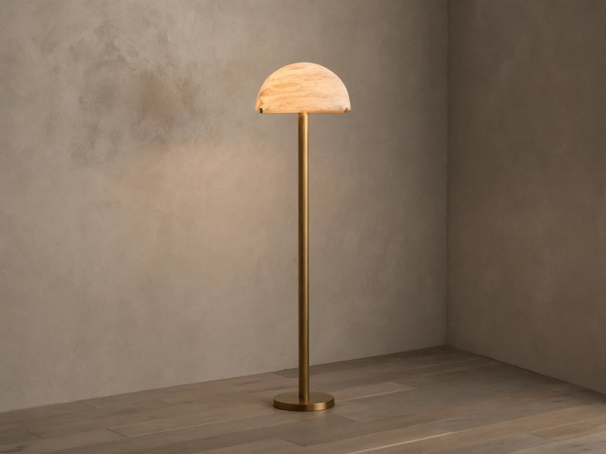 Front view of a brushed brass floor lamp with a half-dome mottled glass shade, emitting a warm glow.