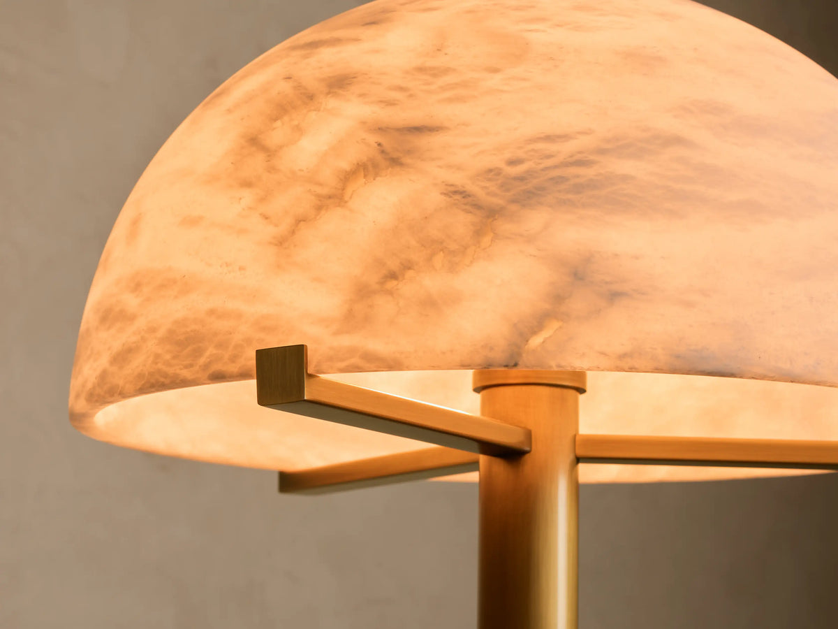 Close-up of an illuminated dome-shaped translucent shade with brown and gray marble-like veining, supported by brass-toned metal.