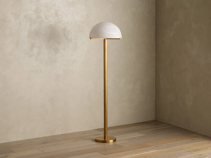 Front view of a brushed brass floor lamp with a half-dome mottled glass shade, emitting a warm glow.