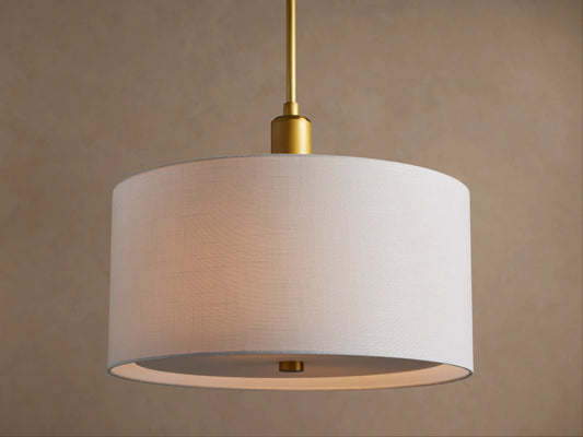 Linden Pendant with a glowing white linen drum shade hanging from a brass rod, seen at a slight angle on a beige background.