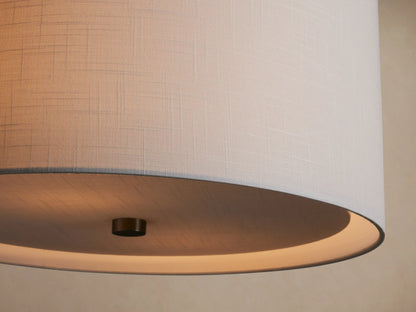 Linden Pendant with a light gray textured linen drum shade and brushed nickel hardware, hanging against a beige wall.