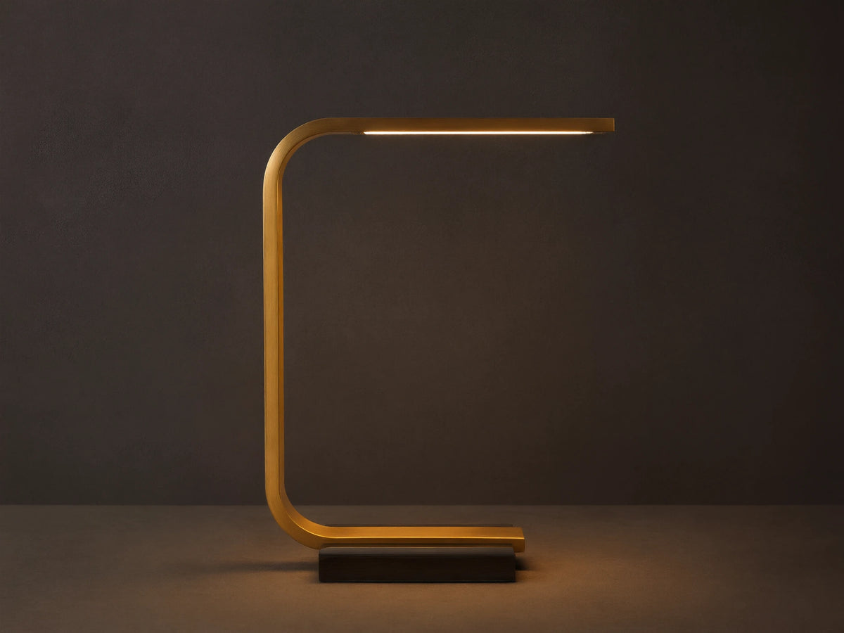 Karson Task Table Lamp: sleek brass, U-shaped lamp with an illuminated LED strip, on a black marble base, resting on a wooden table.