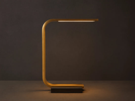 Karson Task Table Lamp: sleek brass, U-shaped lamp with an illuminated LED strip, on a black marble base, resting on a wooden table.