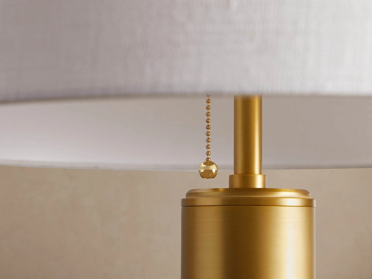 Linden Floor Lamp with a brass-finished pole and round base, topped with a white cylindrical linen shade, standing upright.