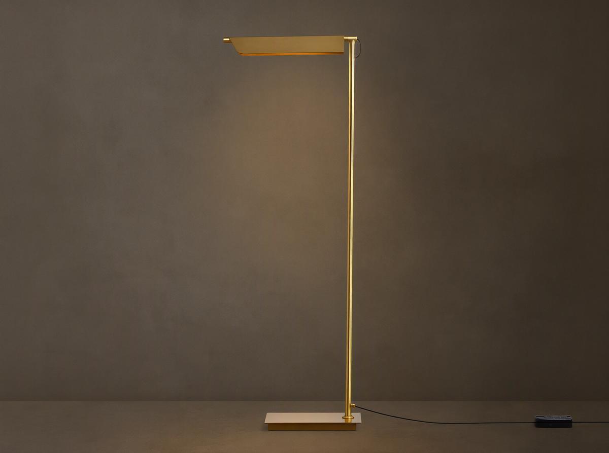 Axle Brass Floor Lamp with a glowing rectangular shade, slim brass pole, square base, and black dimmer on a wooden floor.