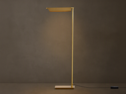 Axle Brass Floor Lamp with a glowing rectangular shade, slim brass pole, square base, and black dimmer on a wooden floor.
