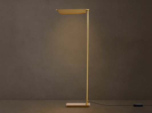 Axle Brass Floor Lamp with a glowing rectangular shade, slim brass pole, square base, and black dimmer on a wooden floor.