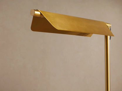 Axle Brass Floor Lamp with a slim brass pole, horizontal rectangular shade, and light square base on a wood floor.