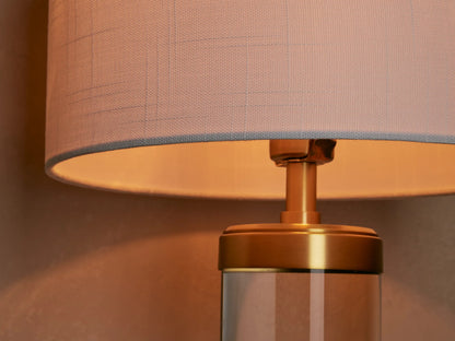 Linden Crystal Table Lamp, upright on wood table. White linen shade, clear crystal column, and brass-finished accents.