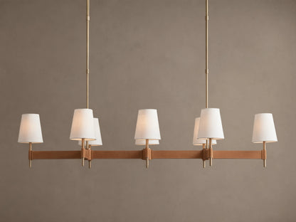 Hastings Linear Chandelier with 6 white linen shades, antiqued brass frame, and brown leather details on a plain wall.