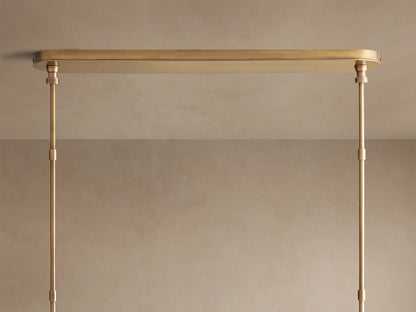 Close-up of Hastings Linear Chandelier with white linen shades, antiqued brass, and brown leather details with white stitching.