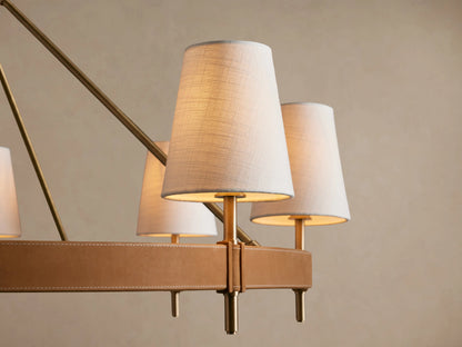 Hastings Round Chandelier with antiqued brass frame, brown leather accents, and eight white linen shades, hanging.