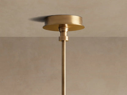Close-up of the Hastings Round Chandelier, showing antiqued brass, tan leather with stitching, and two lit white linen shades.