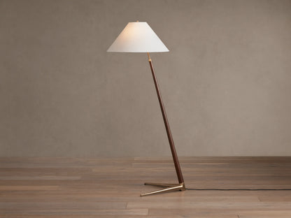 Edric Floor Lamp: Angled walnut wood pole with conical white linen shade and gold brass tripod base on wooden floor.