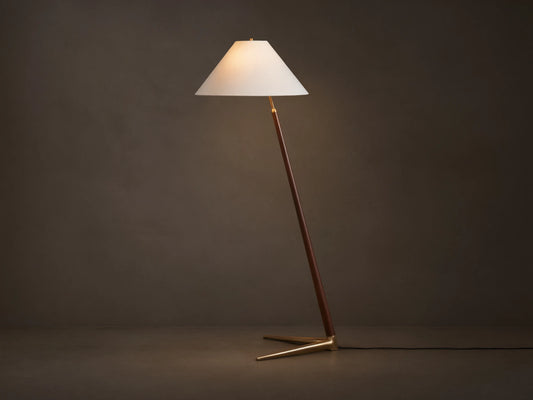 Edric Floor Lamp: Angled walnut wood pole with conical white linen shade and gold brass tripod base on wooden floor.