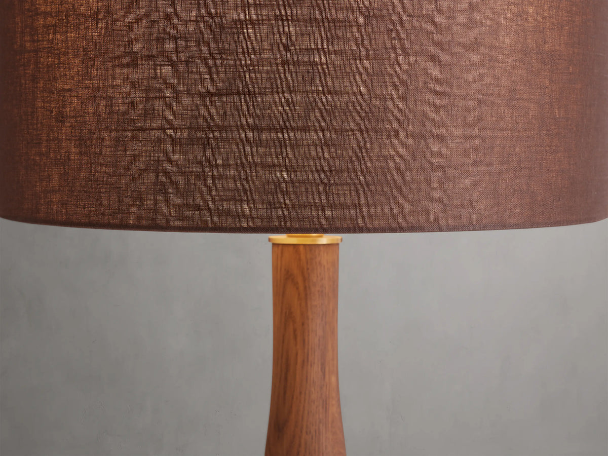 Jonas Table Lamp with twisted oak wood base, brass accents, and brown linen shade on wooden surface against white background.