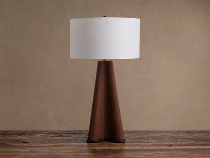 Volant Table Lamp: conical dark oak wood base, brass accent, and cream linen shade, illuminated on a rustic wooden table.