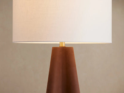 Volant Table Lamp: Tapered dark brown oak wood base with brass accent, topped with a white cylindrical linen shade. On a rustic wood table.