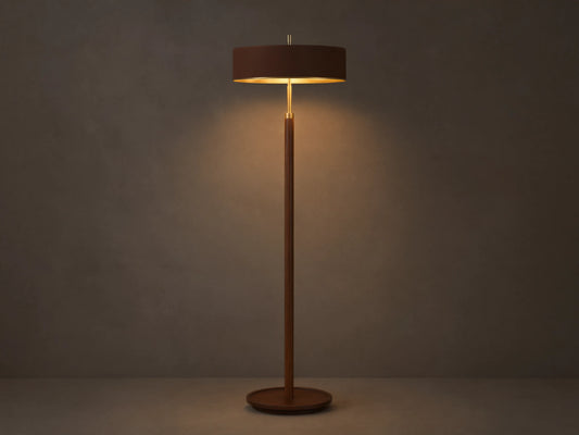A modern floor lamp with a brown cylindrical shade and slender wooden stand, casting warm light on a wooden floor and neutral wall.