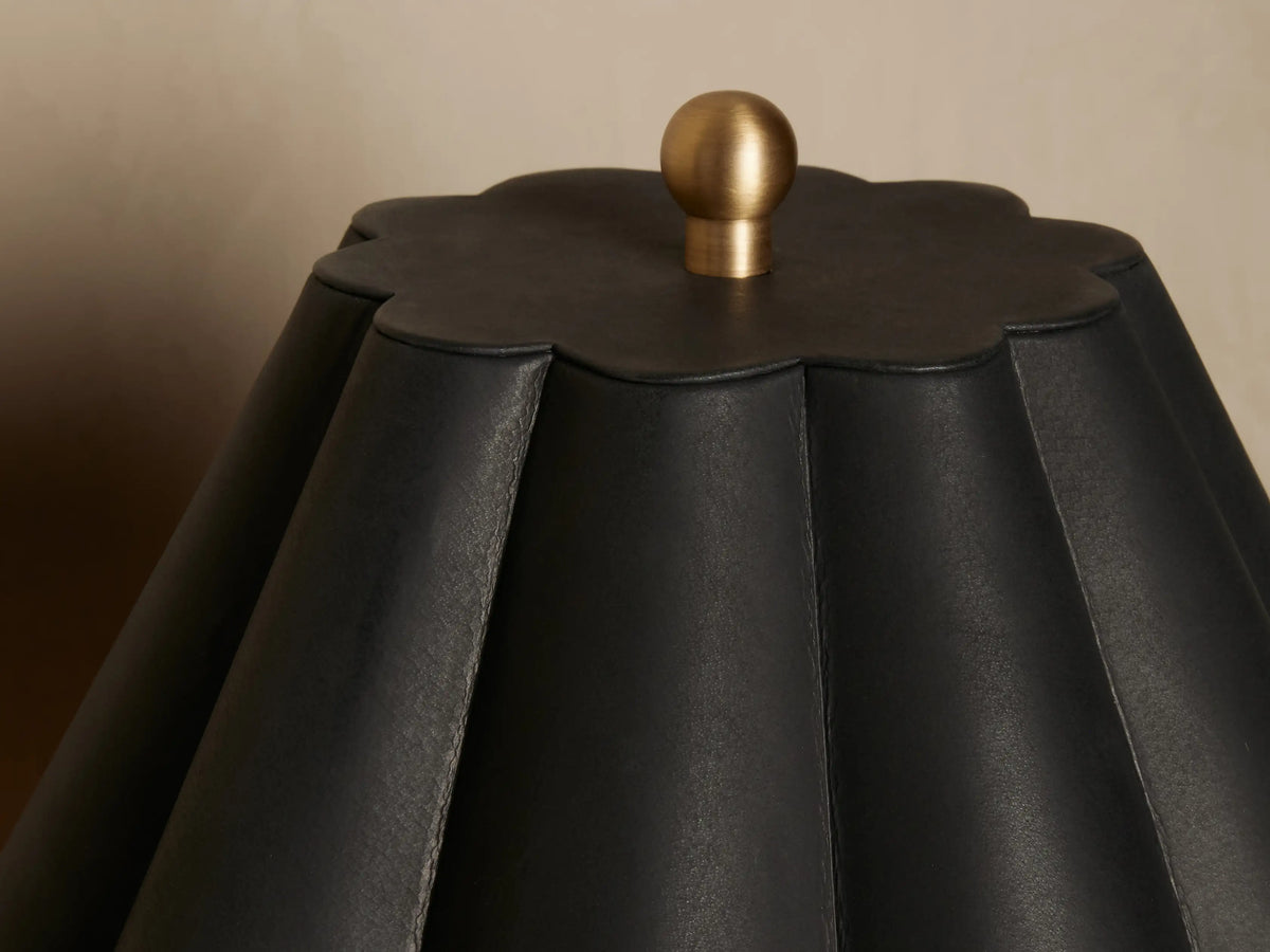 Close-up of Lucy Accent Table Lamp with a scalloped black leather shade & round brass finial on top, against a soft background.