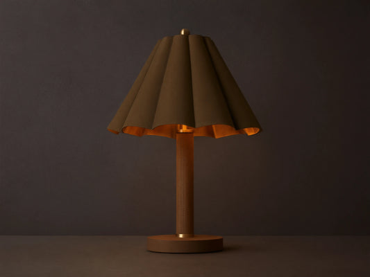 Lucy Accent Table Lamp with pleated dark brown leather shade, gold interior, and tan leather base on a wooden table, emitting a warm glow.
