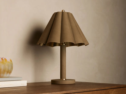 Lucy Accent Table Lamp features a pleated tan leather shade and cylindrical base, sitting on a wooden table next to books and a vase.