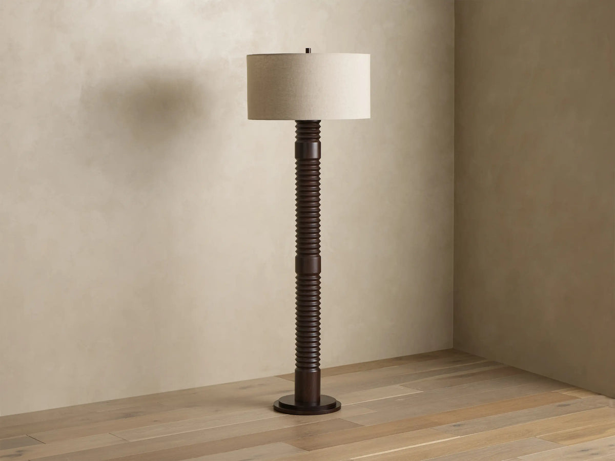 Front view of a dark brown ribbed floor lamp with a cylindrical beige fabric shade, emitting a warm glow.