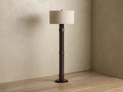 Front view of a dark brown ribbed floor lamp with a cylindrical beige fabric shade, emitting a warm glow.