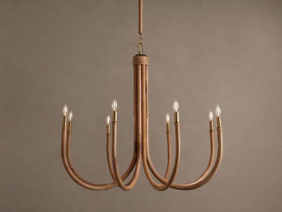 Ravda Round Chandelier features 8 curved rattan arms with brass details, holding glowing clear bulbs, hanging against a brown wall.
