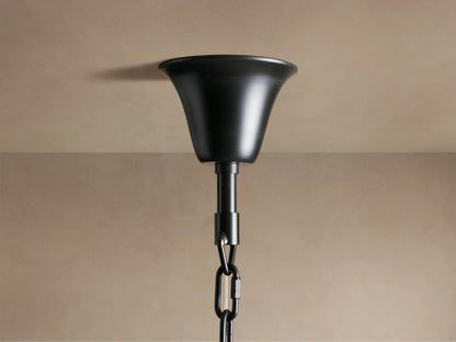 A close-up of a black metal ceiling fixture with a chain attachment against a beige ceiling and wall background.