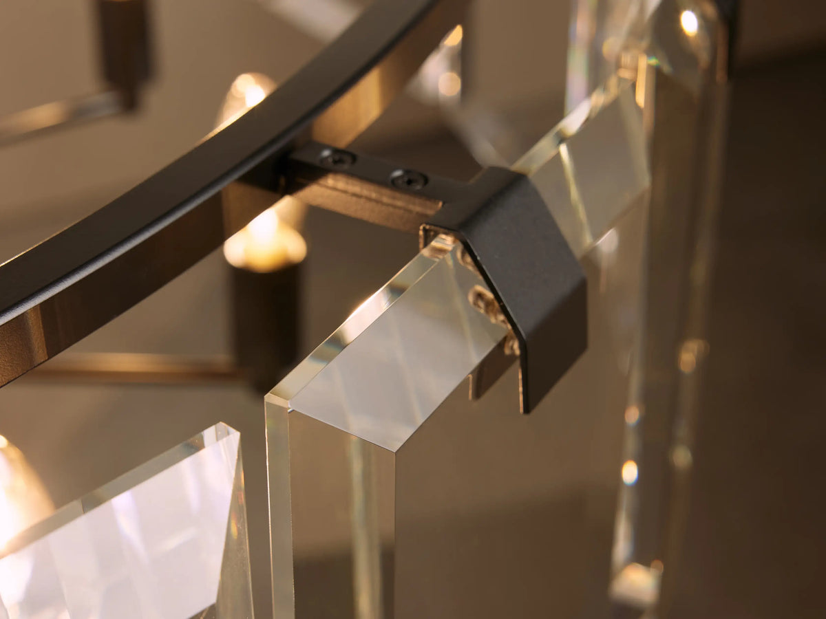 Close-up view of a modern chandelier featuring clear glass panels and a metal frame with a dark finish, illuminated by warm lights.