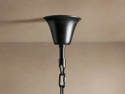 A black metal ceiling mount with a bell-shaped canopy and a link chain extends downward against a beige background.