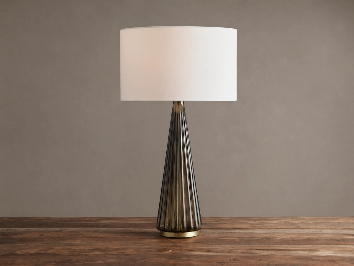 Elisabetta Table Lamp: upright, white linen shade, smoky fluted glass base, brass accent, sitting on a wooden table.